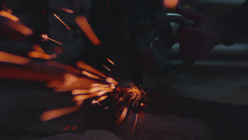 Sparks fly from cutting metal with angle or electric grinder. Metal turning disc cuts the material. Detail shot of cutting iron with circular saw. Welder is working steel at industrial plant.