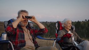 Man with grey beard offers compact binoculars to smiling senior woman. Male pensioner guides hand position and points focus wheel keeping gentle pace at rest - Powered by Shutterstock - Get 15% off with code: PIKWIZARD15
