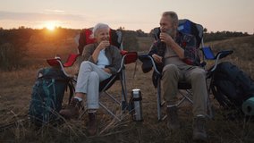 Senior couple sits in camping chairs drinking hot tea at twilight beside ridge. Mature man lifts cup and senior woman takes sip drink enjoying moment at sunset - Powered by Shutterstock - Get 15% off with code: PIKWIZARD15