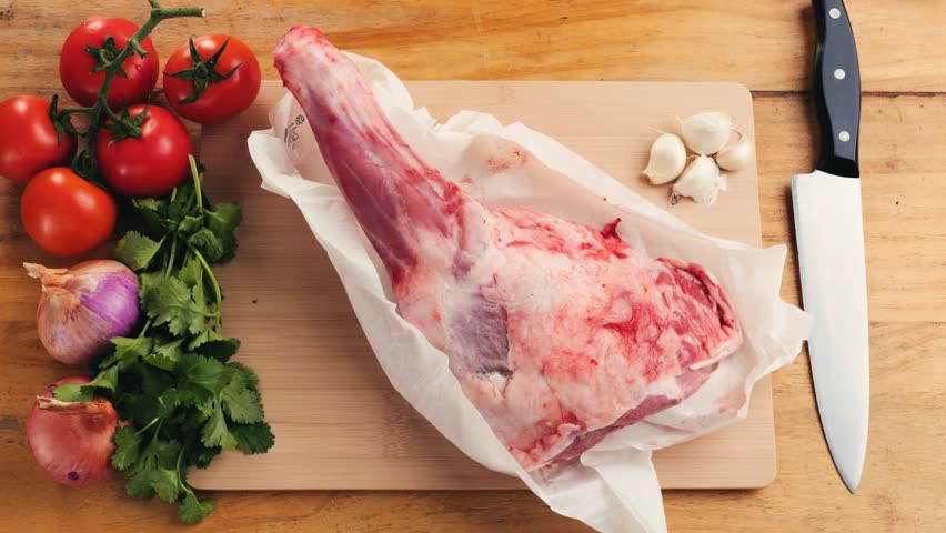 Fresh Raw lamb meat leg with herbs and spices, mutton meat. Chef cooking cutting meat for dinner in restaurant, cafe. Work with knife on kitchen.