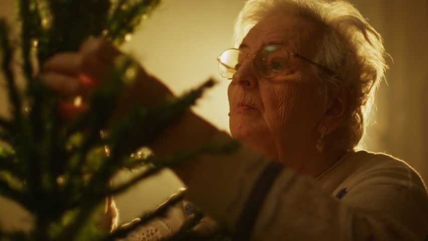 Joyful old woman decorates a festive Christmas tree in cozy home setting