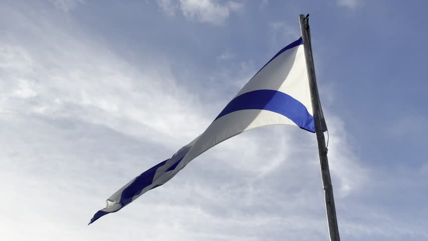 Close-up video of a calmly waving Nova Scotia flag on a flagpole. The sky is blue with a few clouds in the background and the light is warm. The scene is viewed from below.