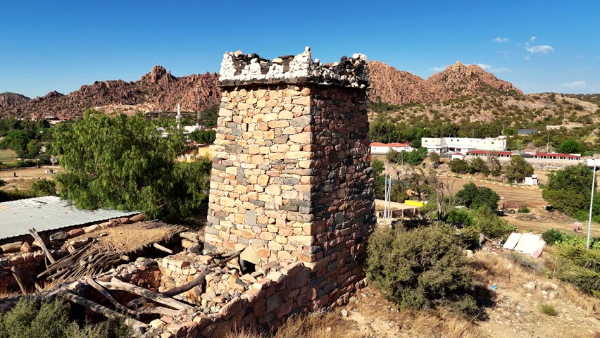 Aerial view of an ancient stone fortress tower in the Asir region of Saudi Arabia. The historic structure stands amid mountains and traditional villages, showcasing the rich Arabian heritage 4k video
