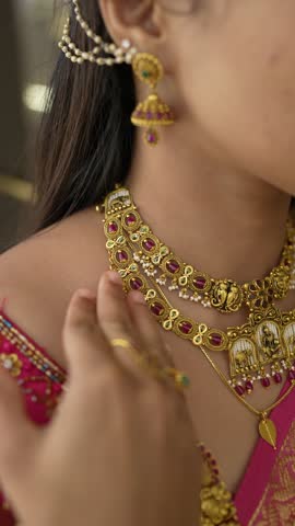 Extreme close-up vertical 4K video of a woman in traditional attire showing gold necklaces and chains with her right hand in a Jewellery store.