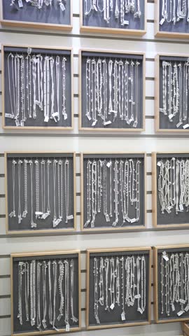 Panning camera view of multiple platinum-silver jewellery chains arranged on a shelf.