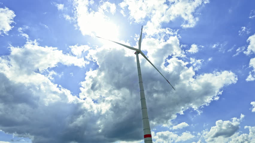 A powerful windmill generates energy against a blue sky. A wind turbine spins against a sky. Energy generation by wind turbines.