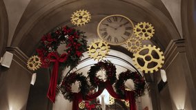 festive wreaths, ornate hallway, festive hallway. Christmas decorations featuring pine wreaths, bright red bows, and metallic gears frame vintage clock in warmly lit hallway. - Powered by Shutterstock - Get 15% off with code: PIKWIZARD15