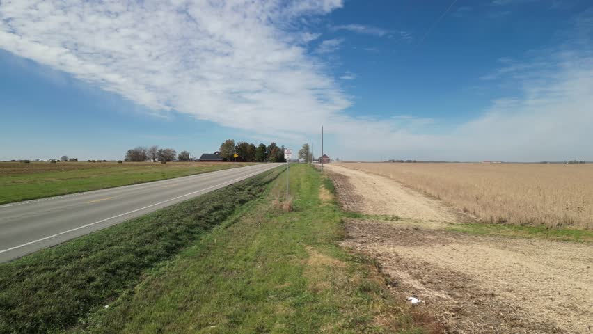 Fly up along a stretch of highway in the fall time in Iowa. Soybean fields on one side, baled hay on the other. A perfect fall Iowa day with blue sky as far as the eye can see. 4k, drone