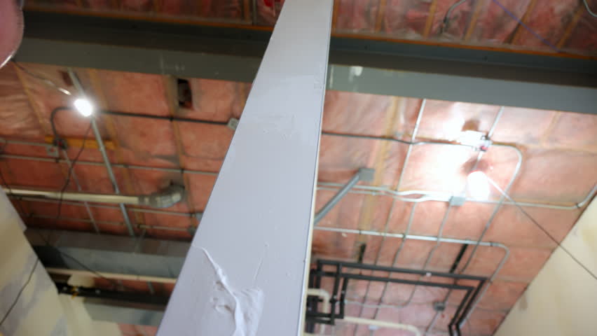 construction worker applies joint compound to drywall end using a metal taping knife. Worker smoothing seams and preparing the surface for finishing
