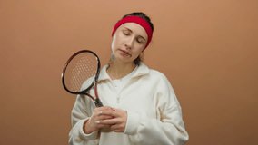Woman wearing red headband holding tennis racket against brown background looking frustrated - Powered by Shutterstock - Get 15% off with code: PIKWIZARD15
