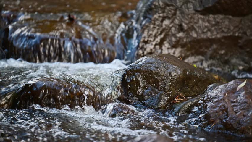 A stream of water is flowing over a rock. The water is clear and the rock is large