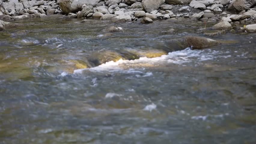 Fast-flowing river water moves over large rocks, forming small waterfalls and splashes. Blue and white water, motion blur in foreground.