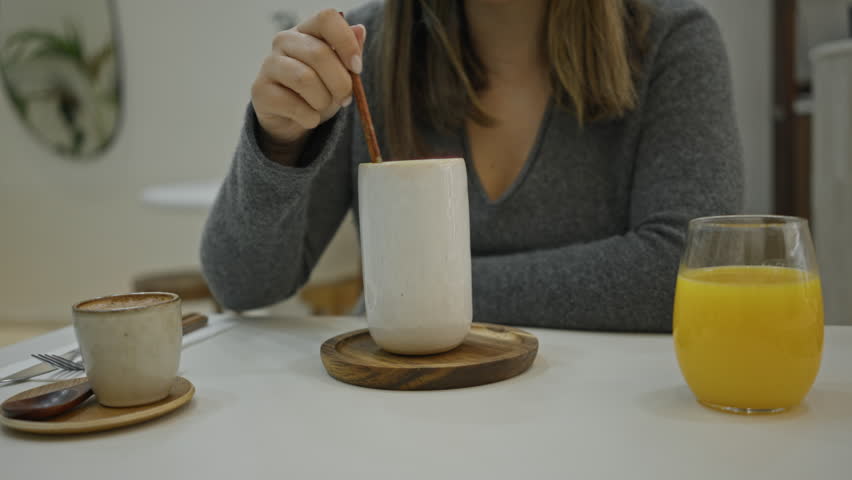 Woman having coffee in a modern luxury restaurant stirring her drink while seated indoors with orange juice beside her on a white table.