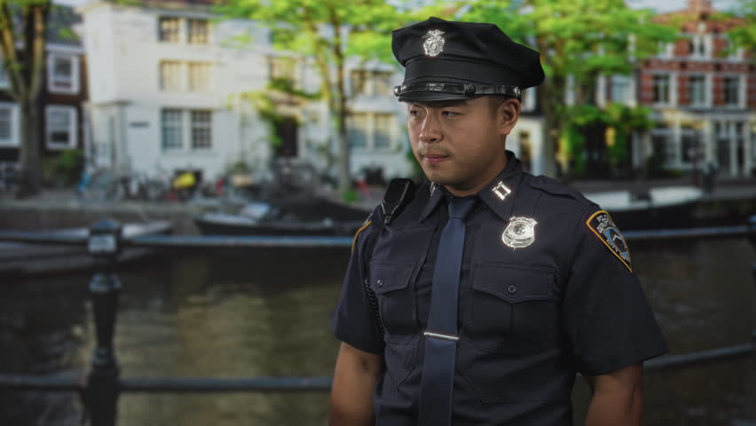 Man policeman biting fingernails by canal railing near building in city under sunlight; anxiety tension fear concern.