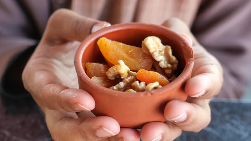 Close-up of a hand holding a small clay bowl filled with walnuts and dried apricots 4k