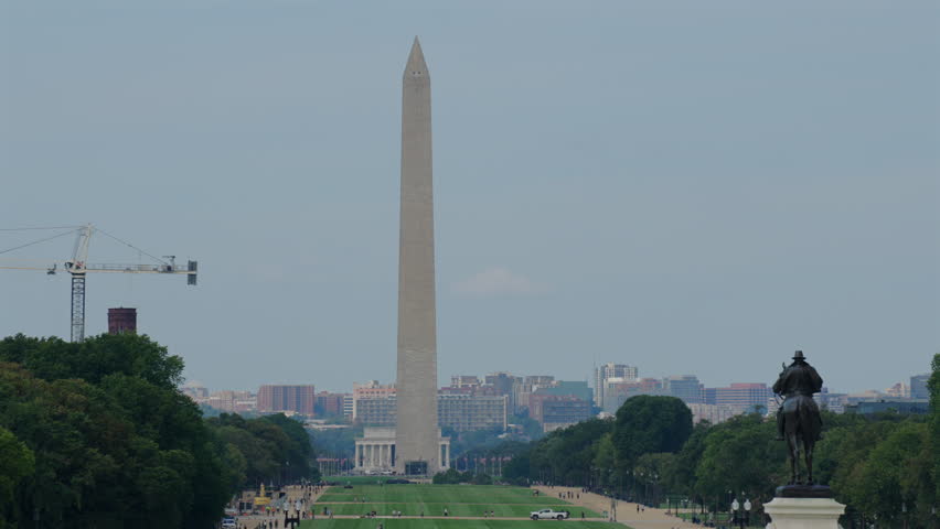 Centered view of Washington Monument flanked by trees and city skyline in background, statue in foreground, static shot, Washington, D.C.