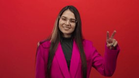 Young woman in pink blazer making peace sign over vibrant red background confidently smiling. - Powered by Shutterstock - Get 15% off with code: PIKWIZARD15