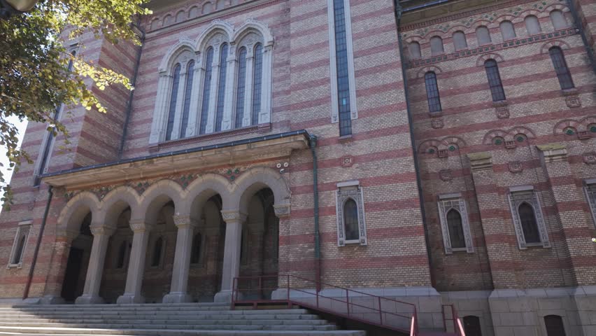 Tilt-up footage of the Metropolitan Cathedral in Timisoara, Romania, with trees in the foreground adding depth and natural framing.