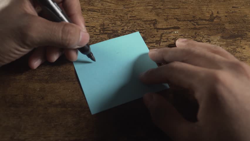 Close up of a person's hands writing the motivational phrase one day at a time on a sticky note