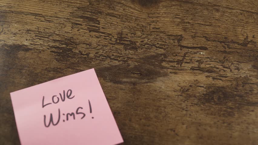 Hand placing several pink sticky notes with positive, romantic handwritten messages on a wooden table