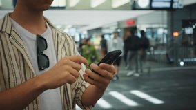 Young man views his smartphone, Man in striped shirt uses phone amid busy terminal scene, Young individual in casual attire interacts with mobile device amidst bustling transportation hub - Powered by Shutterstock - Get 15% off with code: PIKWIZARD15