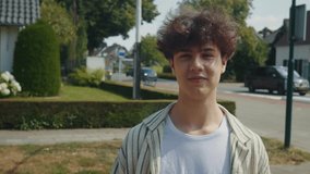 Smiling young man portrait on suburban street bright daytime with greenery and houses behind, direct eye contact, approachable expression and relaxed stance, ideal for lifestyle and profile - Powered by Shutterstock - Get 15% off with code: PIKWIZARD15