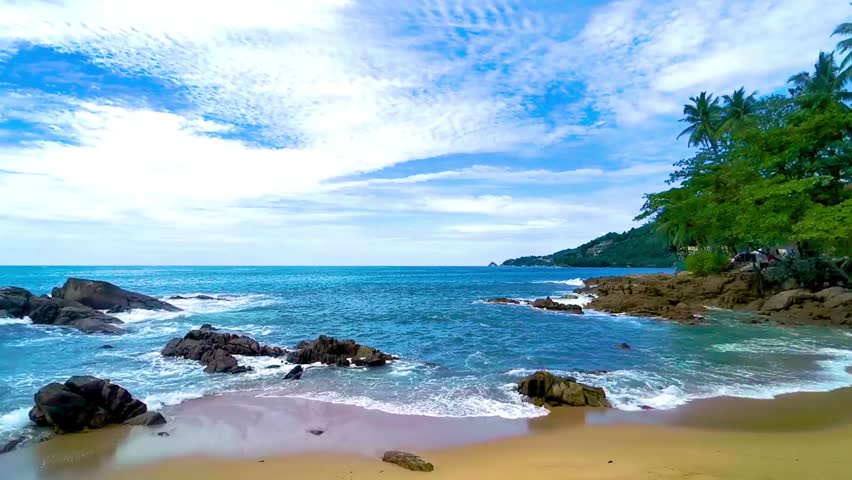 Amazing rocky Kalim Beach tropical landscape panorama view with blue sky turquoise water waves palm trees and rocks in Patong Beach Kathu Phuket Island Province Southern Thailand in Southeast Asia.