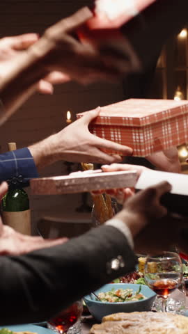 Vertical slow motion video hands exchanging gift boxes over festive dinner table concept christmas holiday celebration friendship gratitude joy cozy home warm light family gathering