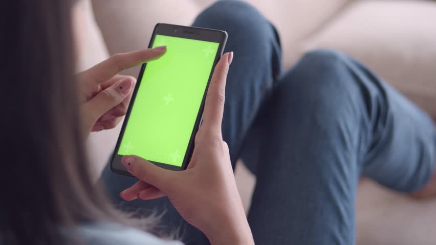 Close up hands holding chroma key mobile phone at home. woman watching green screen cellphone resting couch. man using mockup smartphone lying sofa at weekend room. Technology Internet social media
