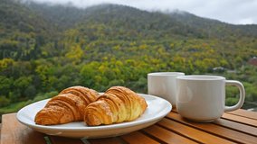 Pouring coffee. A plate of croissants and two cups of coffee sit on a wooden table overlooking a mountain - Powered by Shutterstock - Get 15% off with code: PIKWIZARD15