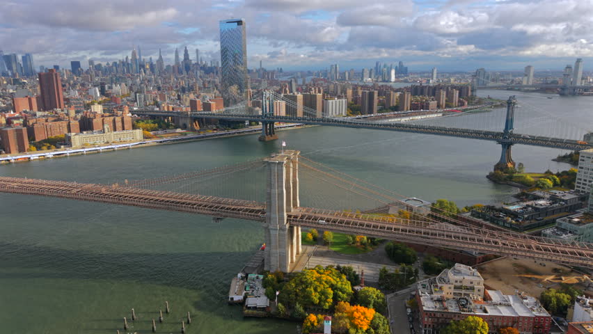 Cinematic aerial daylight shot over Brooklyn Bridge and Manhattan bridge with Manhattan New York City skyline, NYC view from above, Drone footage showcasing fall scenery along urban New York riverbank