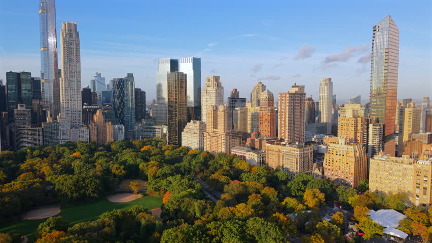 Breathtaking Drone shot over New York City Central Park with colorful trees in autumn, surrounded by the towering skyline of midtown Manhattan on a sunny clear blu sky morning. New York, USA