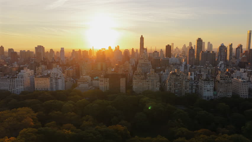 Breathtaking Drone shot over New York City Central Park at sunrise with colorful trees at full, morning light scene of cityscape, tall building stands agains the sun. New York, USA