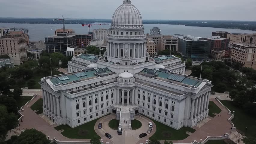 Aerial drone video of a state capitol building in Madison, Wisconsin as the drone flies further back, exposing the lake in the distance.
