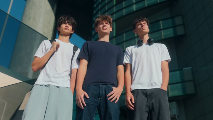 Three friends stylish teenage friends pose outdoors against an urban backdrop. Dressed in casual tees and jeans, they show a mix of relaxed confidence, unity, and modern teen vibes.