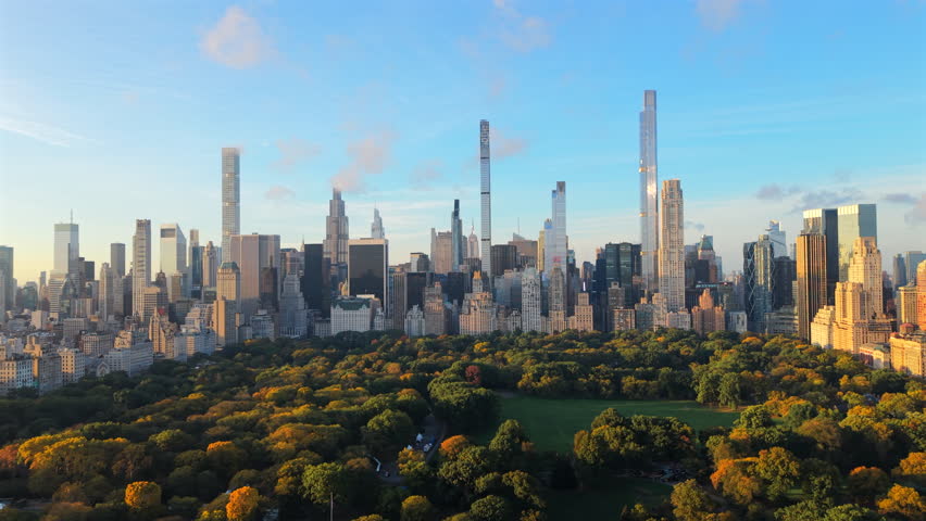 Beautiful aerial shot showing New York City Central Park colorful autumn foliage beneath the illuminated Manhattan skyline during early morning golden hour. Sunrise in a big city. New York, USA