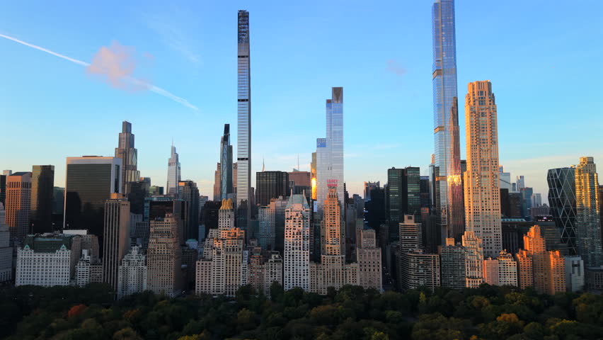Cinematic Aerial footage of Manhattan, New York tall skyscrapers glowing in morning light, with Central Park fall trees in the foreground, New York City skyline. Perfect clear blue sky at autumn time.