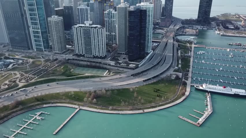 Aerial drone video slowly trucking to the right showing highway traffic next to a lake and boat marina while showing the skyline buildings in downtown Chicago, Illinois.