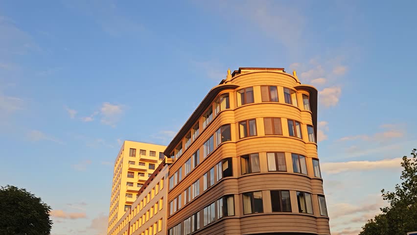 Walking shot of a curved corner apartment building in warm sunset light with golden reflections on the windows