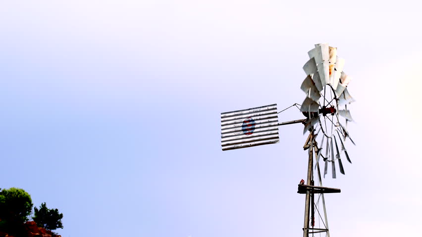 Old rusty windmill spinning in wind pumping up water on farm, slow motion