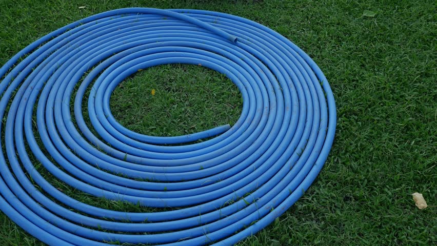 Blue Water Hose Coiled in Spiral Pattern on Green Grass Lawn - Garden Equipment and Yard Work.