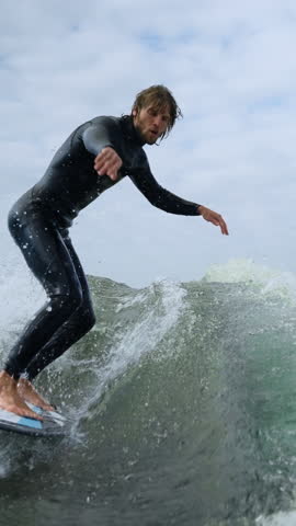 A skilled surfer expertly rides a powerful wave, showcasing balance and agility on the surfboard against a backdrop of cloudy skies and ocean spray.
