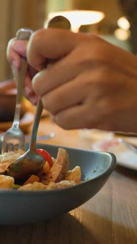 Hands mix spicy Thai noodle salad in restaurant, natural lighting, close-up, shallow depth of field