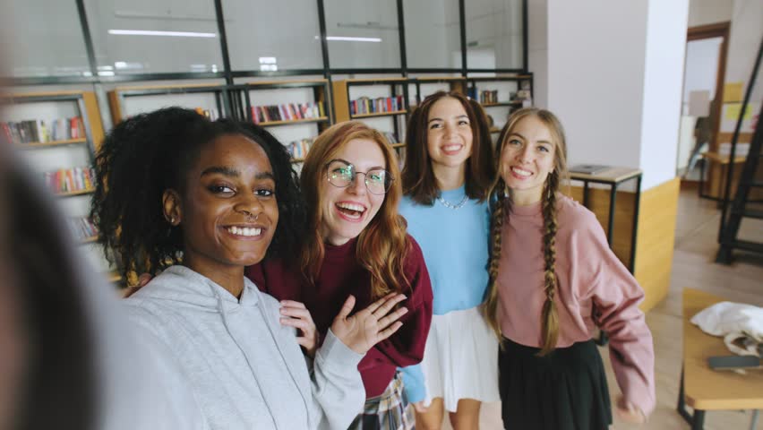 POV Four multiracial friends gather in a spacious library, laughing and posing happily for a selfie. They showcase their unique styles and the joy of being together during their leisure time.