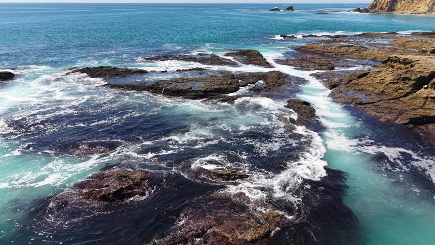Aerial view of ocean waves crashing against rocky tidepools along the rugged coastline of Laguna Beach, California