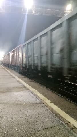 A freight train rushes through the night under bright, glowing lanterns. Sound inside.