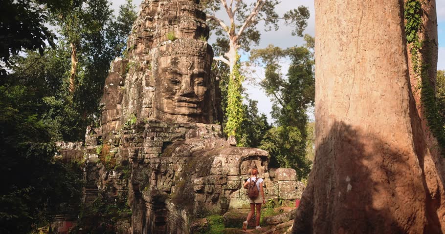 Young backpacker admiring Bayon temple stone face tower in Angkor Wat, Cambodia. Ancient Khmer ruins in lush jungle. Concept footage for tourism, history, culture, and world travel inspiration.