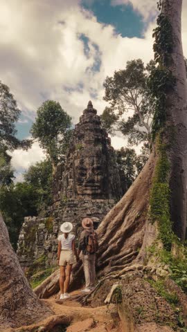 A man and woman in casual travel outfits explore Victory Gate with giant tree roots near Bayon Temple, Angkor Thom, Cambodia. Cinematic lifestyle and tourism clip ideal for heritage and promo content.