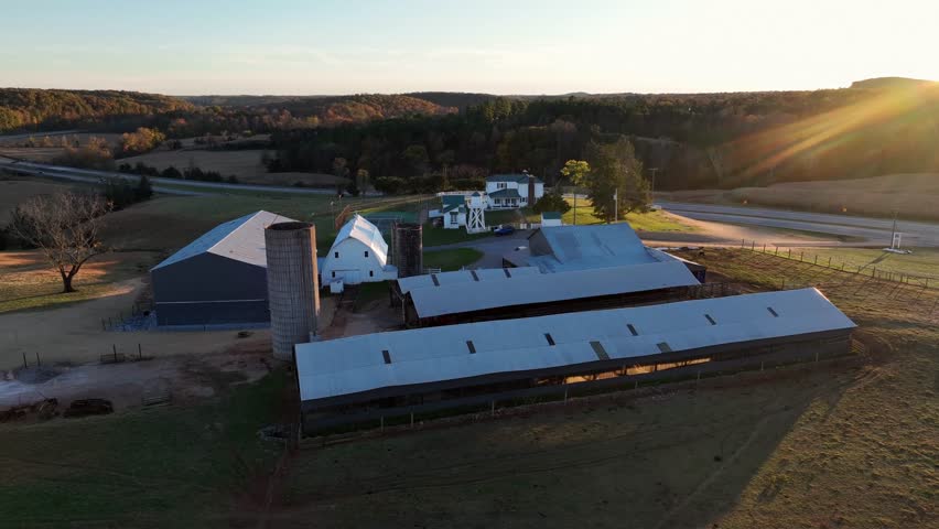 American Countryside in fall season at sunset time. Aerial approaching shot. Traditional farmsteads and houses in rural suburb of town. Quaint and quiet landscape. Barn and silo storage.