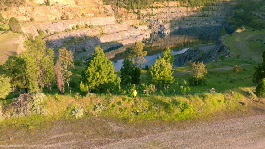 Aerial view of quarry filled with water, surrounded by tiered rocky walls and lush green trees, creating a striking contrast of textures and tones, Adelaide, South Australia, Australia.
